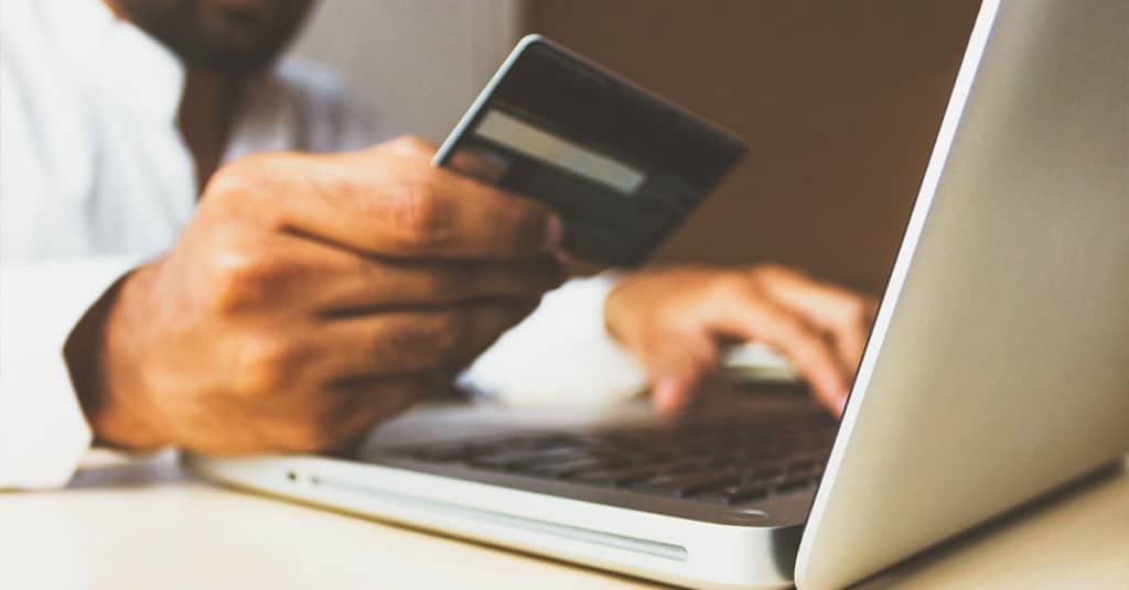 Man's hand holding credit card and typing on a laptop